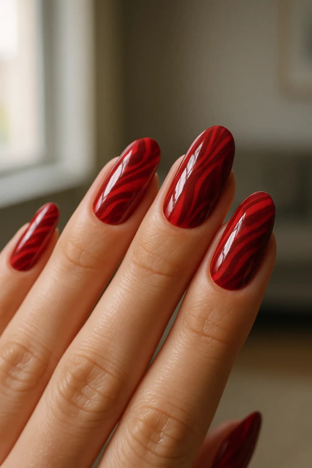 Close-up of long oval nails painted red with various intricate patterns reflecting natural light.